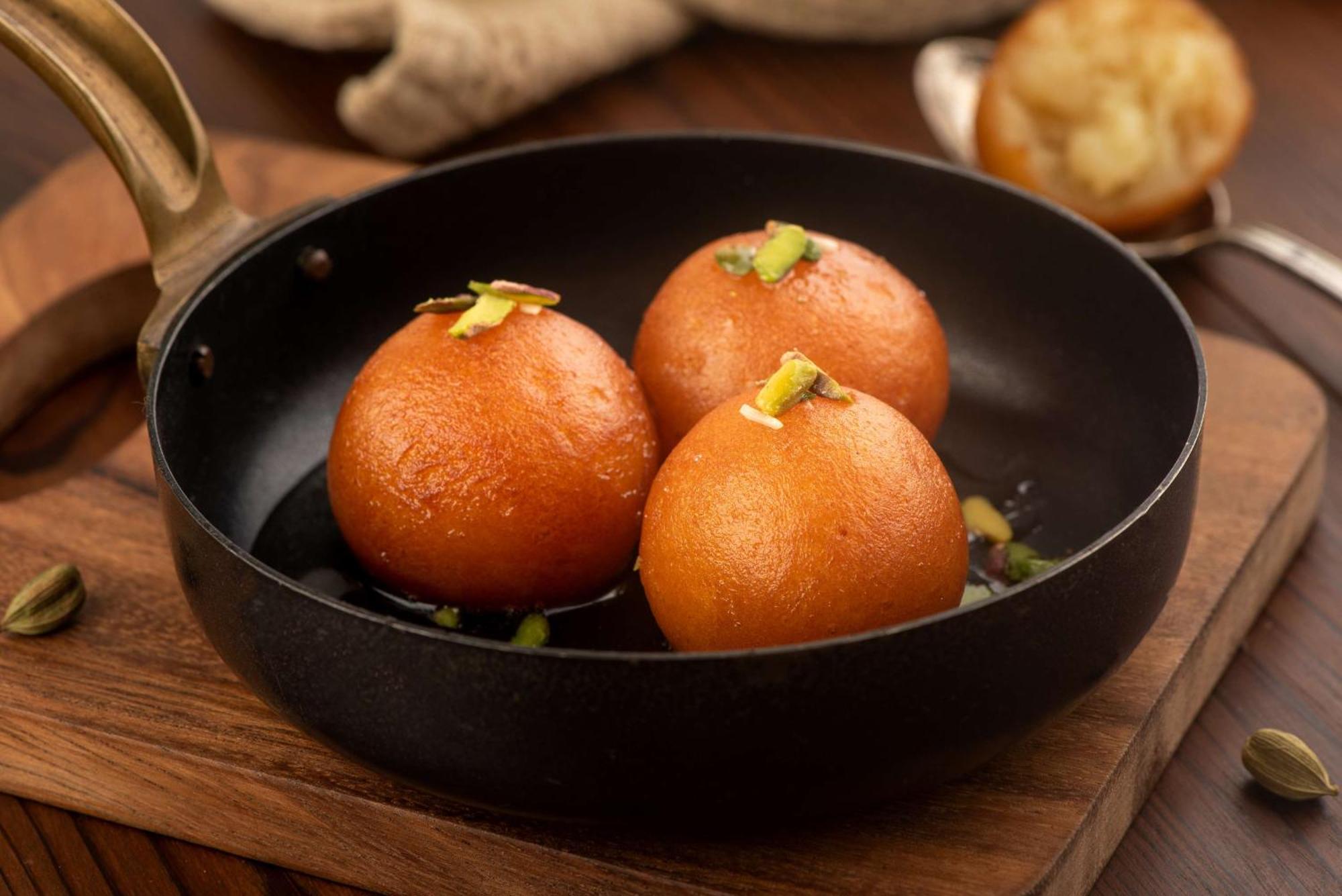 Hotel Radisson Blu Plaza Delhi Airport Nowe Delhi Zewnętrze zdjęcie The photo shows three round, golden-brown sweets sitting in a small black frying pan. These sweets are likely Gulab Jamun, a popular Indian dessert made from milk solids, sugar, and flavored with cardamom and rose water. They are garnished with piece